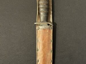 Vintage combat knife with leather sheath and metal guard.