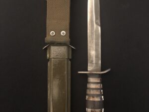 A vintage combat knife with a leather sheath on a dark surface.