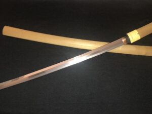 A traditional Japanese katana with a wooden sheath on a black surface.