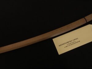 A wooden sword with a plaque on display against a black background.