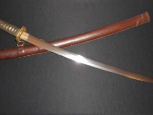 A curved sword with a wooden handle and sheath on a dark surface.