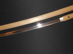 A polished katana blade with a wooden sheath on a black background.