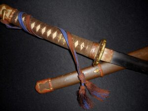 Close-up of a decorative dagger with a wrapped handle and tassels on a dark background.
