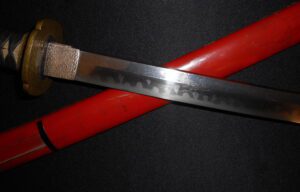 Close-up of a sharp katana blade with a red sheath.