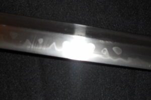 A close-up of a metal blade with engraved text on a dark background.