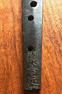 Close-up of a metal tool with Japanese inscriptions on a wooden surface.
