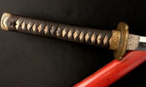 Close-up of a katana handle with intricate diamond pattern wrapping and a red sheath.
