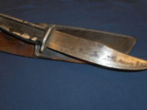 Close-up of a vintage hunting knife with a leather sheath on a blue surface.