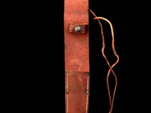 A vintage red leather knife sheath with a strap on a black background.