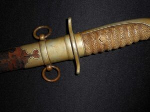 Close-up of an antique brass dagger handle with intricate grip and scabbard rings.