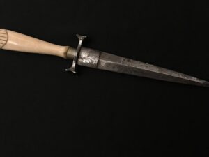 Hand gripping an old, rusty dagger against a black background.