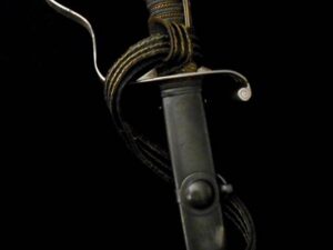Close-up of a vintage dagger with a leather sheath and rope against a black background.