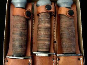 Three leather sheathed knives with wrapped handles in a box.