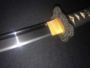 Close-up of a katana blade and ornate handle against a dark background.
