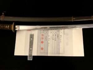 Traditional Japanese katana with detailed paper and ruler beside it.