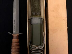 A vintage combat knife with a leather handle and sheath in a box.