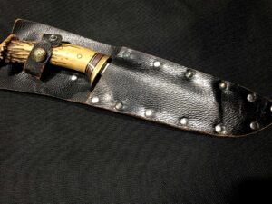 A knife with a decorated handle in a black leather sheath.