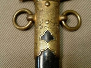 Close-up of a decorative sword or cane handle with engraved details and rings.