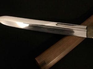 Close-up of a polished katana blade resting on a wooden stand.