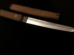 Close-up of a traditional Japanese knife with wooden handle and sheath.