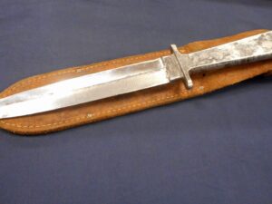 Antique dagger with a leather sheath on a dark surface.
