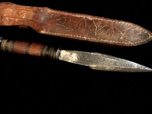A weathered knife with a carved wooden sheath on a black background.