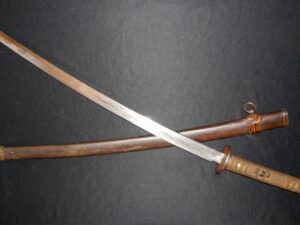 An antique sword with a wooden scabbard on a dark surface.