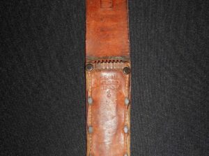 Vintage leather sheath with metal detail on a dark fabric background.