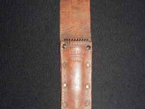 Leather knife sheath with metal rivets on black fabric.