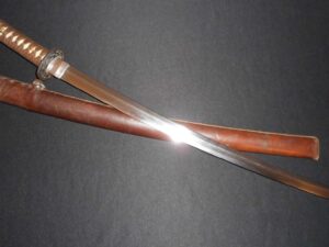 Close-up of a shiny sword blade and wooden scabbard on a dark background.