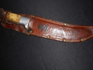 Close-up of a vintage knife with a wooden handle in a worn leather sheath.