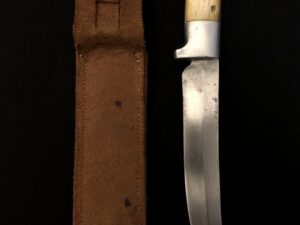 A vintage hunting knife with a bone handle beside its leather sheath on a dark background.
