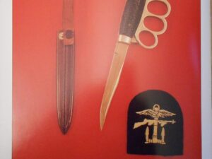 Antique dagger with brass knuckle handle and leather sheath displayed on red background.