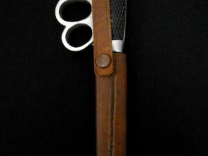 Silver scissors in a brown leather case against a black background.