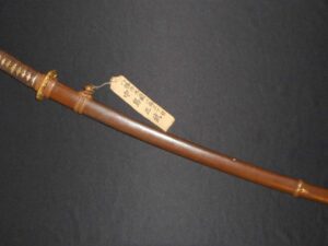 A traditional curved sword with a protective sheath and a labeled tag.