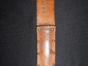 Close-up of a leather sheath with metal rivets on a dark fabric background.