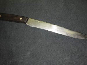 A large kitchen knife with a wooden handle on a dark surface.